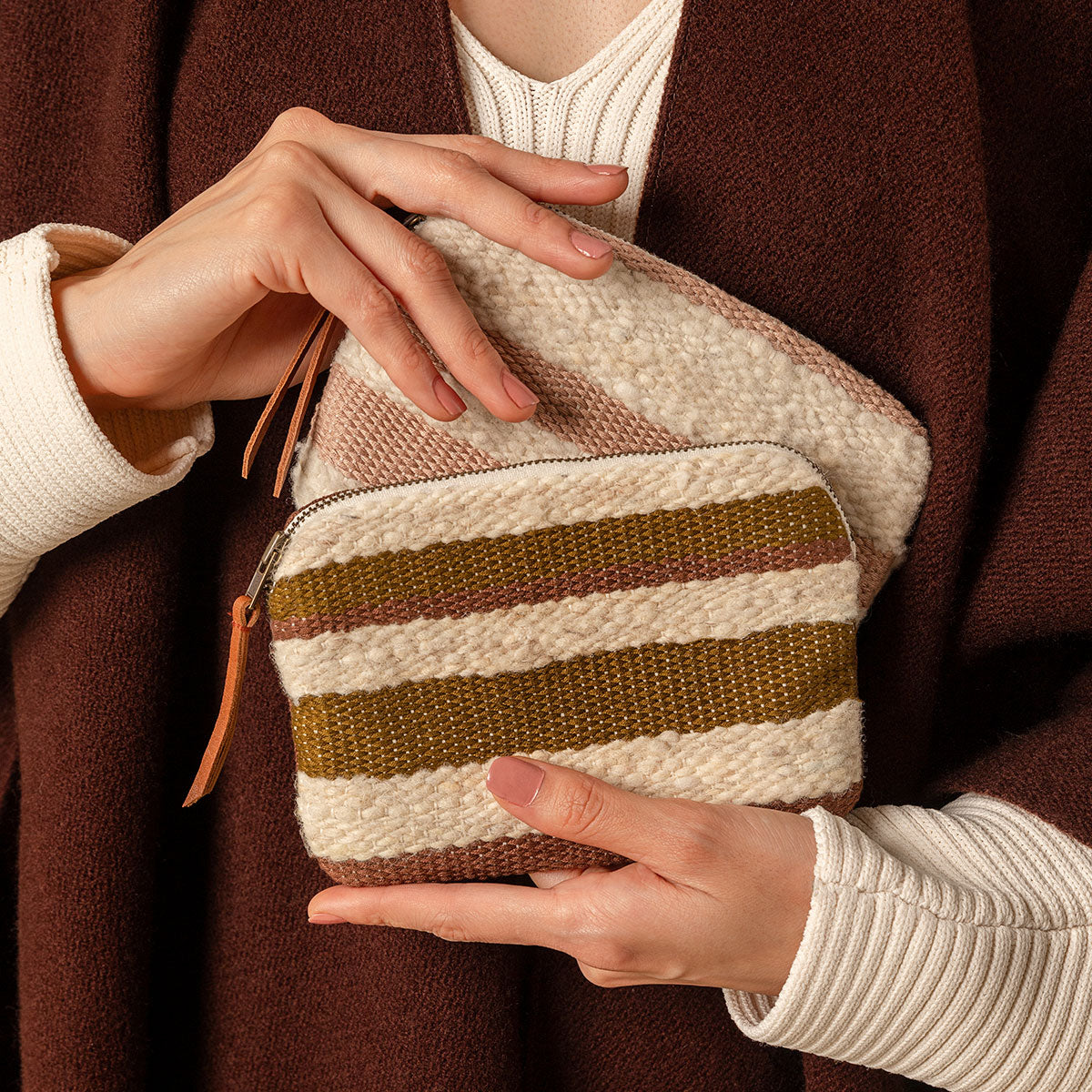 A model holds twoTeresa Wallets in Forest and Snow patterns. The Snow pattern has horizontal pale pink and beige stripes. The Forest pattern has horizontal olive green and beige stripes.