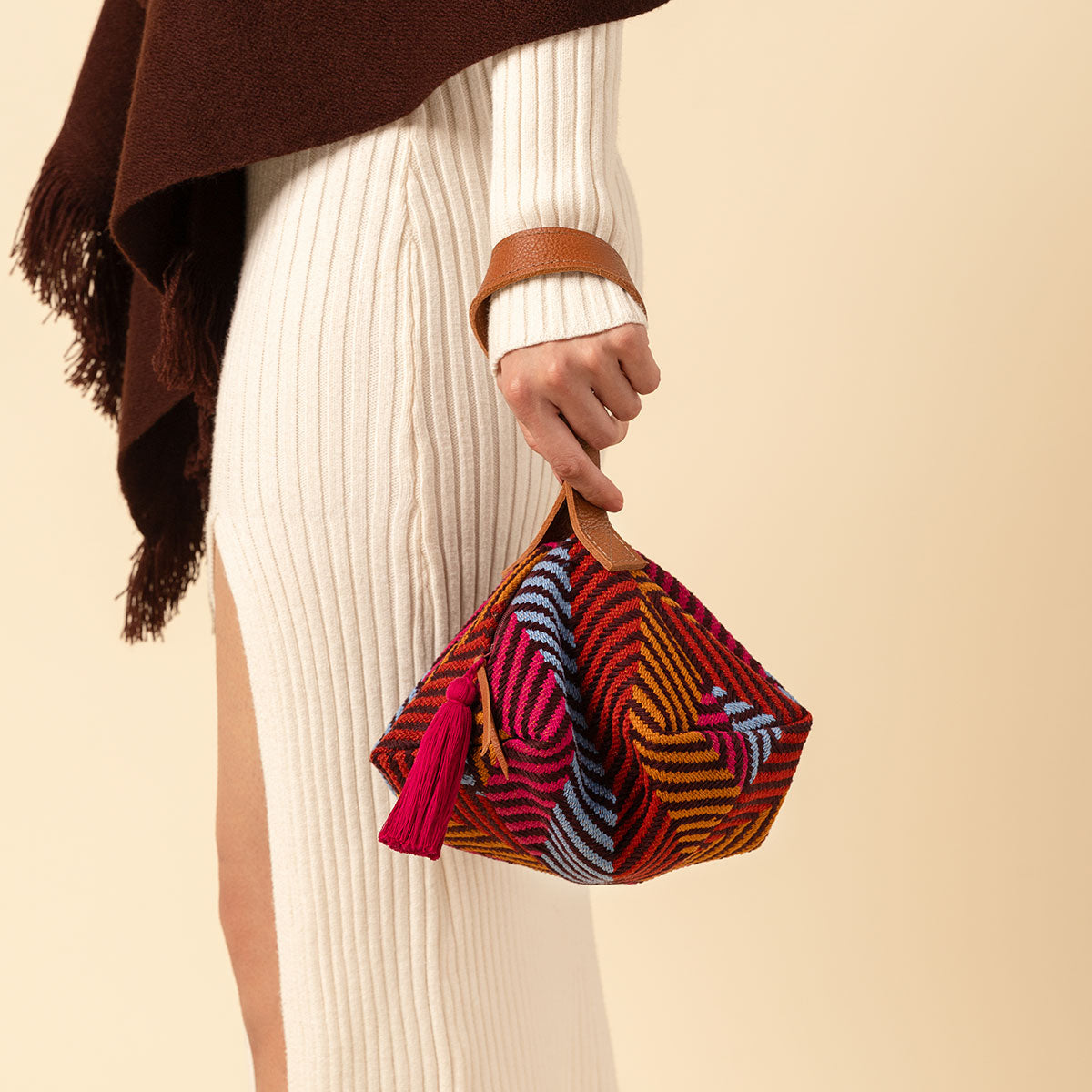 A model holds the Dulce Wristlet in Winter Berry pattern. The Dulce Wristlet has a leather handle and red tassel wiith a red, blue, and ochre yellow fabric pattern.