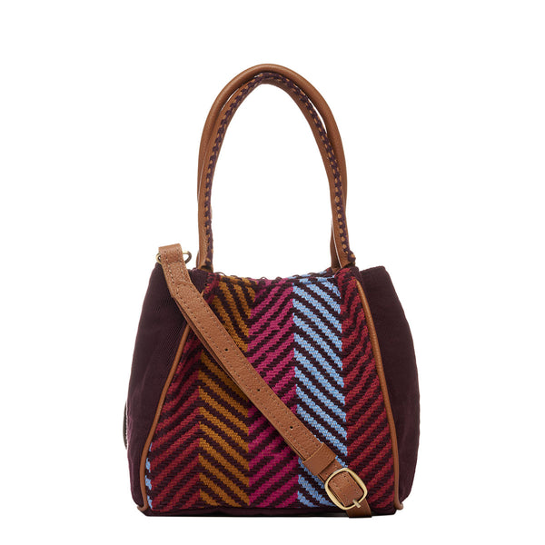 Hand woven artisan Flora Petite Tote in Chestnut shown at the front. The sides of the bag are in solid brown colors. The leather handles have brown embroidered detailing. The Winter Berry pattern has vertical yellow ochre, red, and blue stripes. A leather strap is hung diagonally.