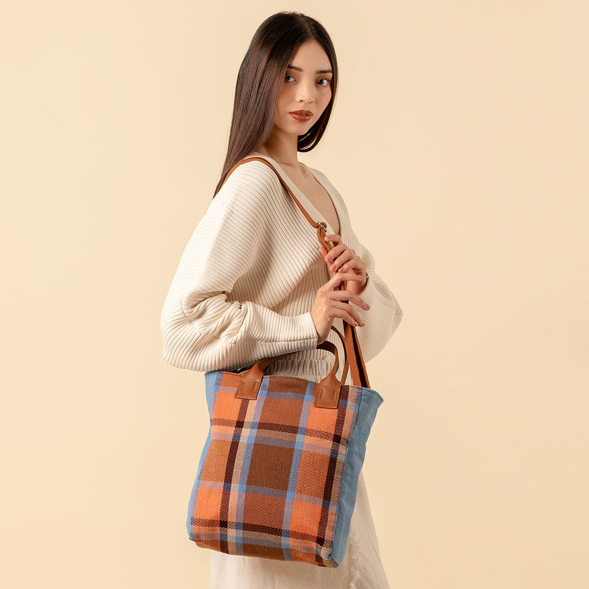 Hand woven artisan Ana Tote in Brickstone pattern. A model wears the extended strap over her shoulder and looks at the camera. The brickstone pattern is a brown, orange, and sky blue plaid.