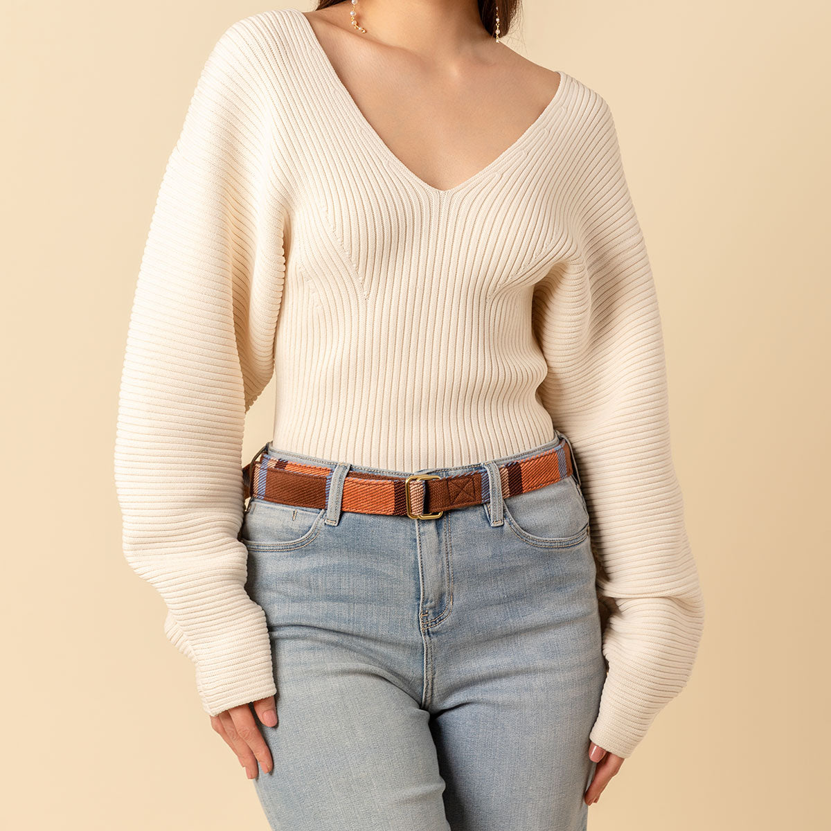 Hand woven artisan Celeste belt in Brickstone color. A model wears the belt and the photo is cropped to show the model's torso and waist wearing the belt. She is wearing a white sweater and light wash jeans.