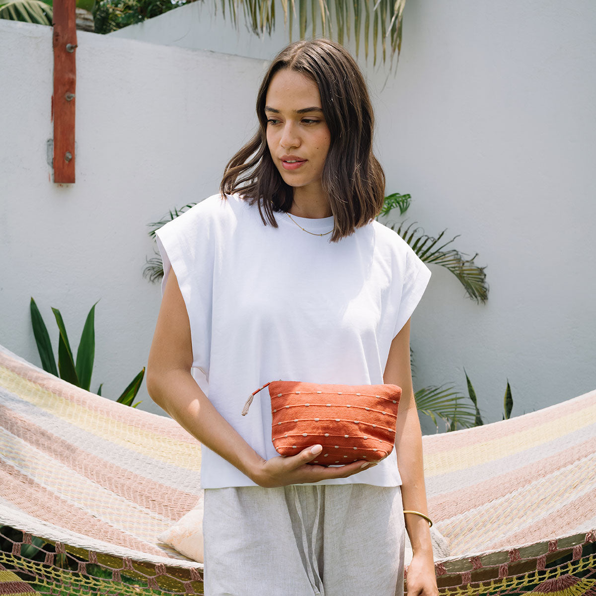 A model holds the Mini Cristina in Desert Sands. The background is a hammock inside an open white-walled courtyard. Plants are around the area.