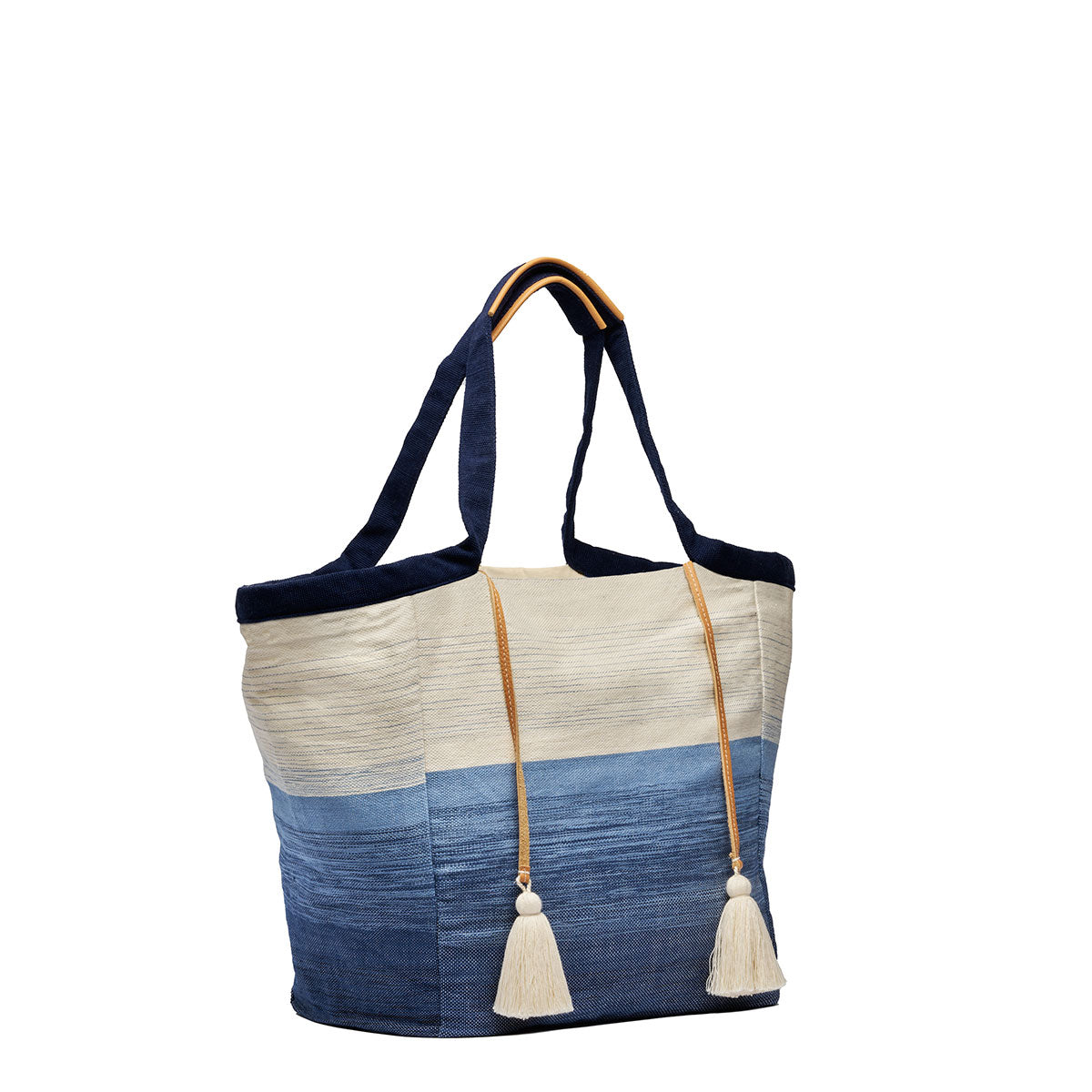 Side view of the Rosa Tote in Ocean Breeze. It has a two-toned fabric, white at the top and blue at the bottom. It has dark fabric handles with leather detailing and two white yarn tassels.