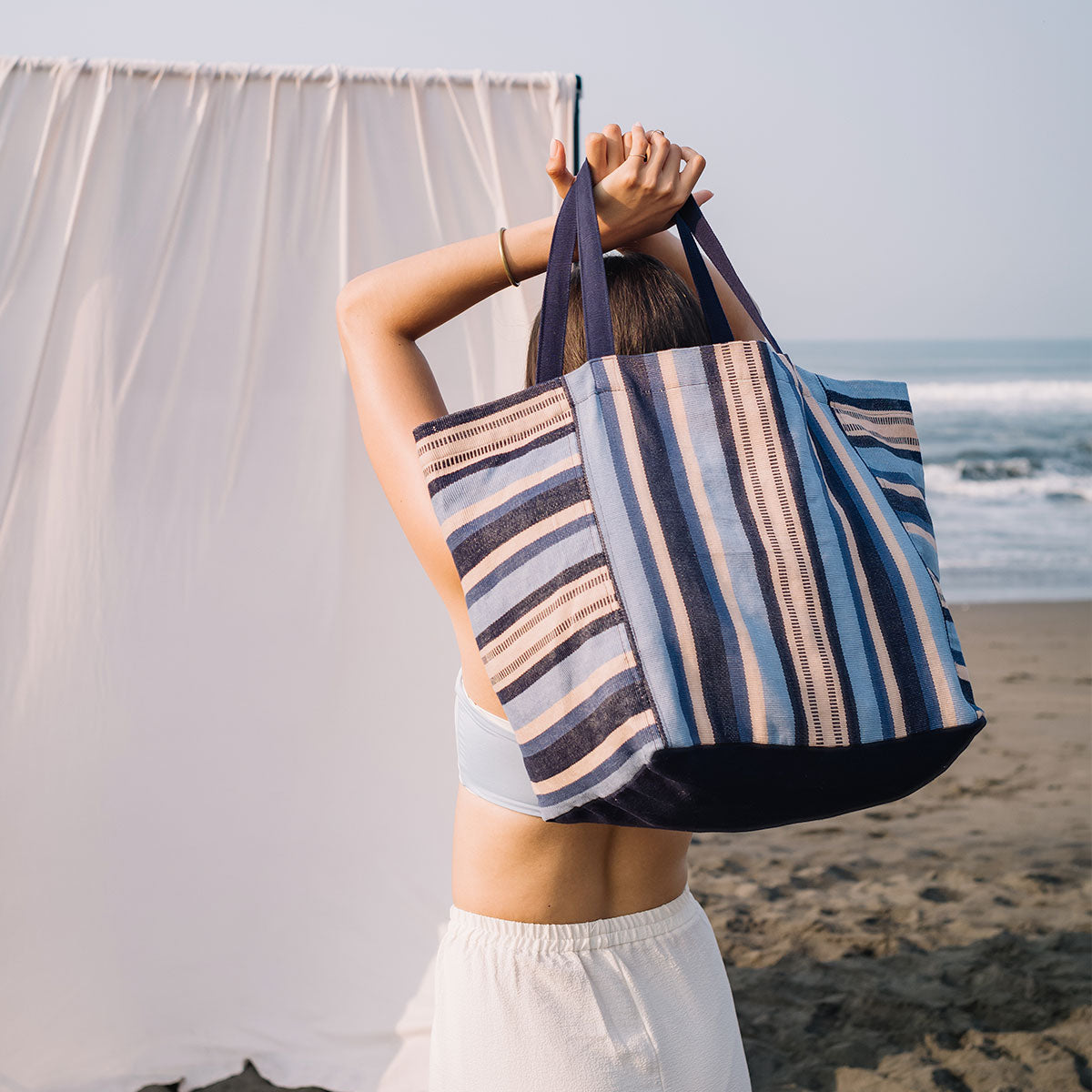 A model holds the Blanca Tote in Skyscape on the beach.