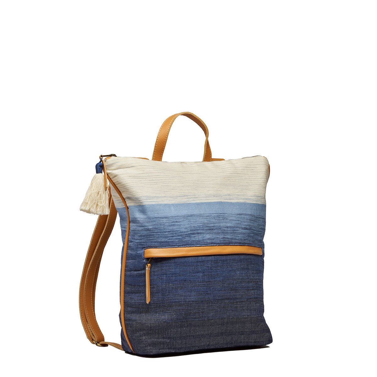 Side angle view of the Lorena Backpack in Ocean Breeze. It has a white to dark blue gradient pattern. It has leather straps and an exterior pocket. It has a cotton tassel.