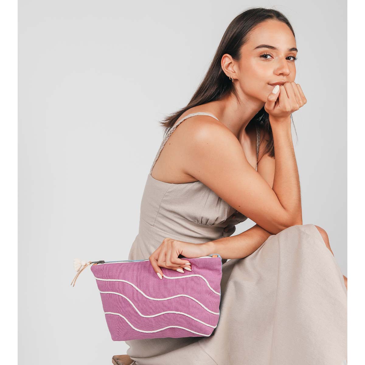 A model sits down and holds the hand woven artisan Cristina Cosmetic Pouch in Cosmic Waves pattern