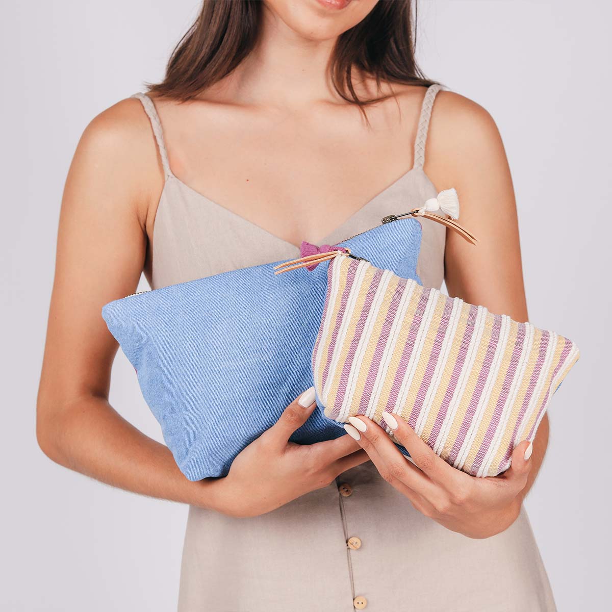 A model holds the hand woven artisan Cristina Cosmetic Pouch in Cosmic Waves and the Mini Cristina Cosmetic Pouch in Cream Soda in both arms.