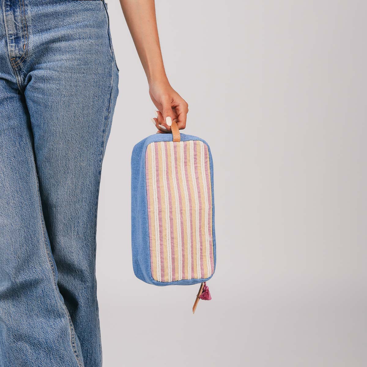 A model holds the leather handle of the hand woven artisan Edna Dopp Kit in Cream Soda