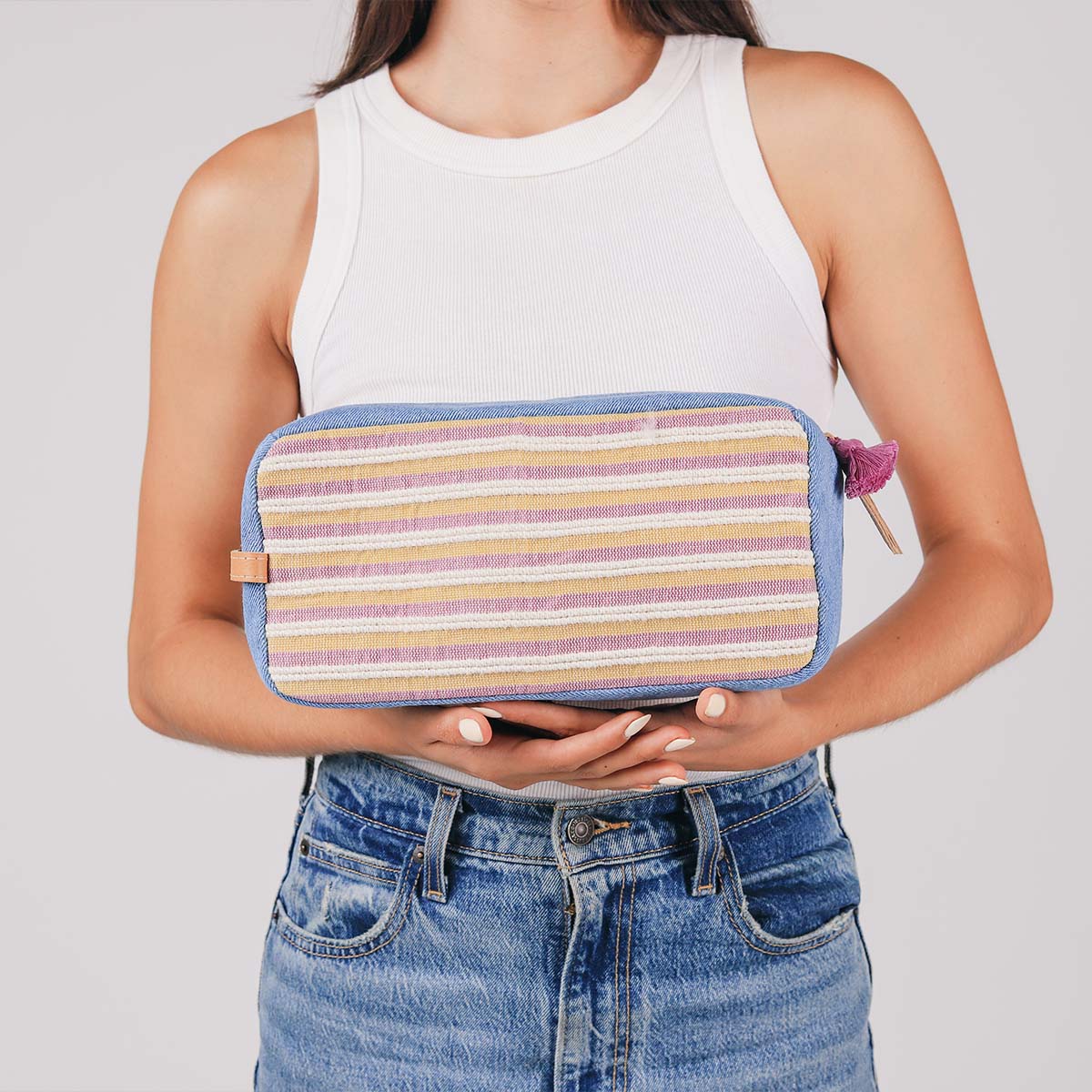 A model holds the hand woven artisan Edna Dopp Kit in Cream Soda in both hands.