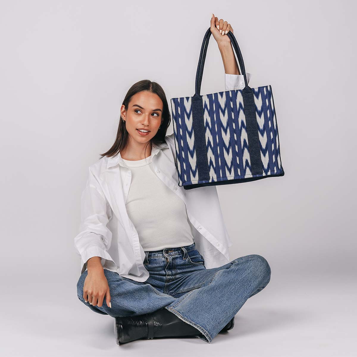 A model sits cross-legged and holds the hand woven artisan Irma Tote in Atitlán Hills over her head.