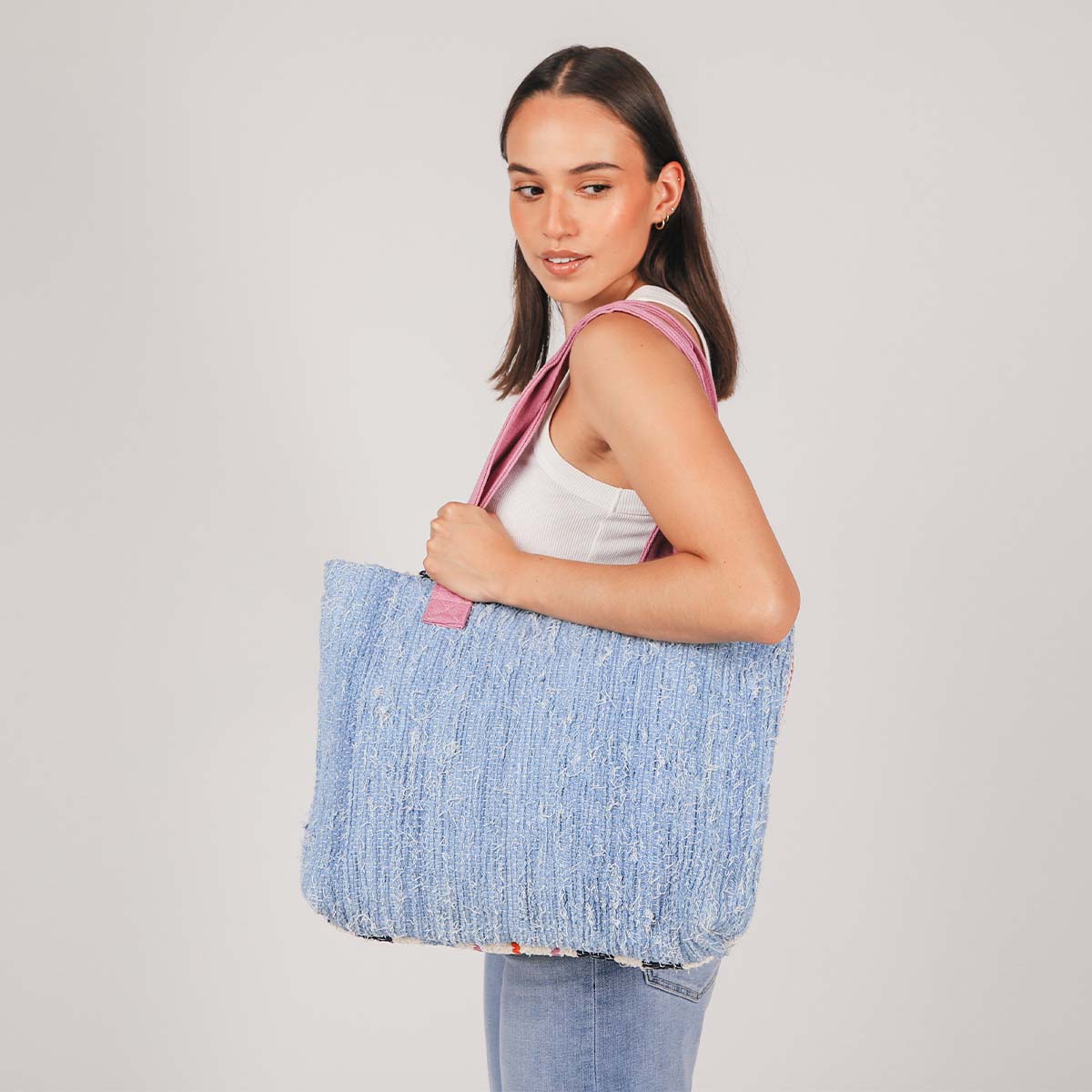 A model holds the hand woven artisan Patricia Interwoven Tote in Spring Sherbert over her shoulder. The side shown has a solid sky blue woven color and pink handles.